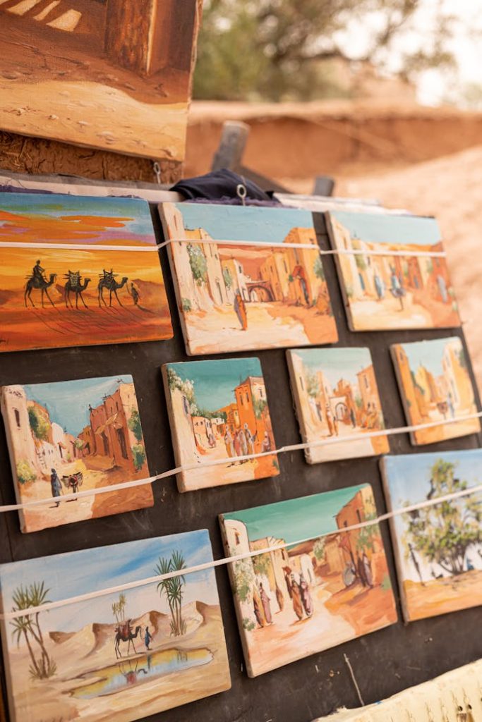 A collection of desert-themed paintings on display at an outdoor market, showcasing vibrant desert scenes.