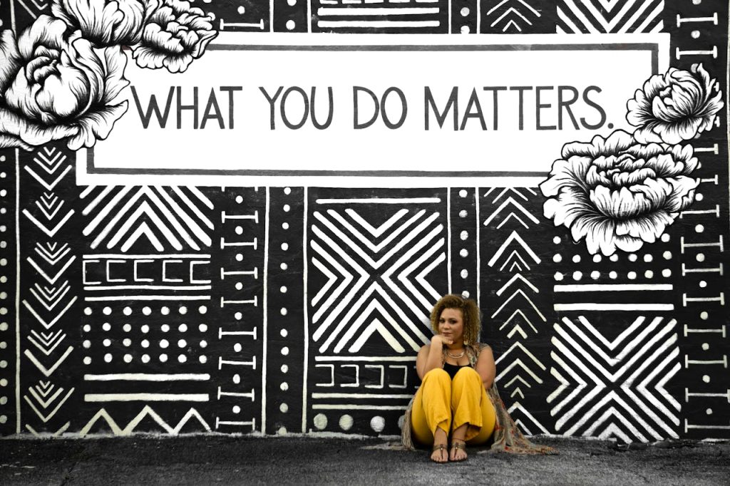 A woman sitting against a motivational mural reading What You Do Matters in Birmingham, AL.